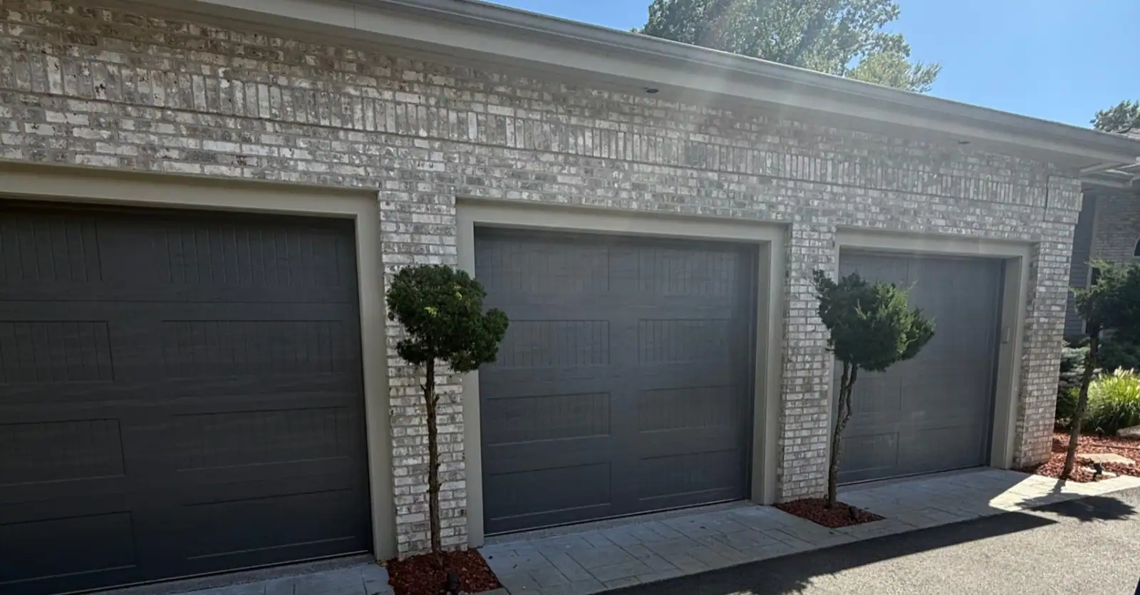 Three dark residential garage doors installed on a brick home in Southern New England